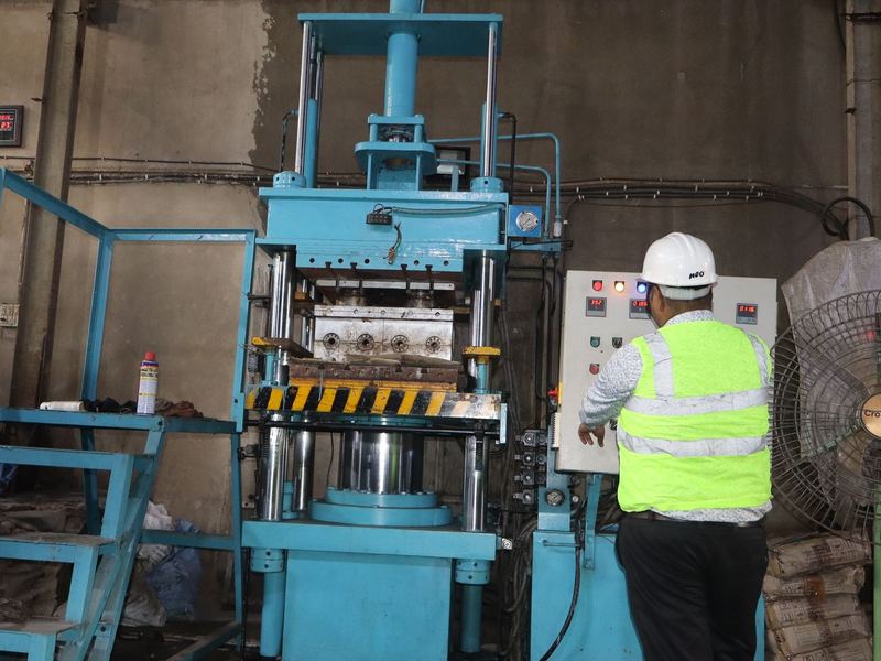 Hydraulic press - operator station. An operator at the hydraulic press control station, in helmet and high-visibility vest.