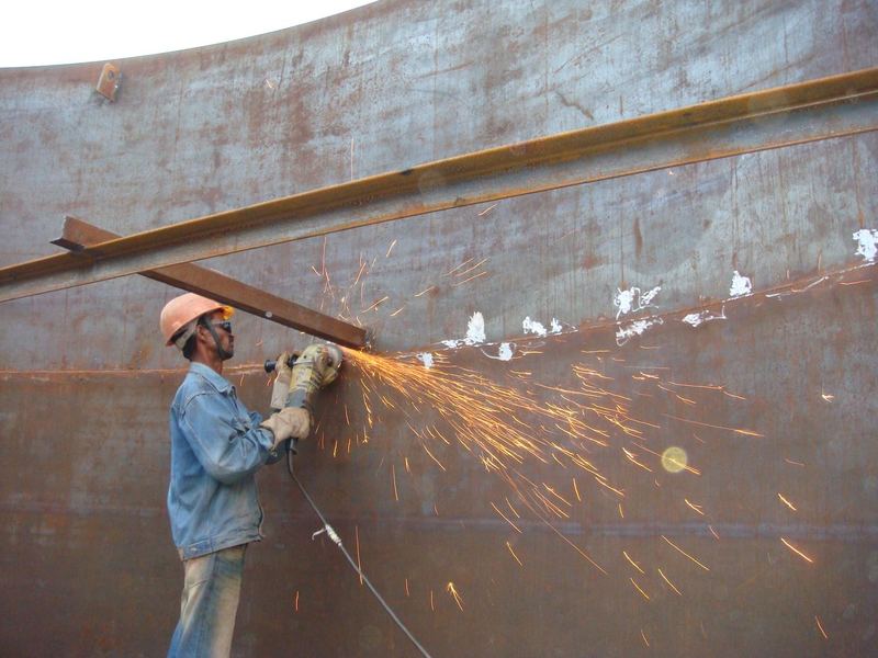 Grinding a weld. Dressing a weld on a fabricated plate section. Helmet, eye protection and gloves; welding is to IS 816 and AWS D1.1, inspected to IS 822.