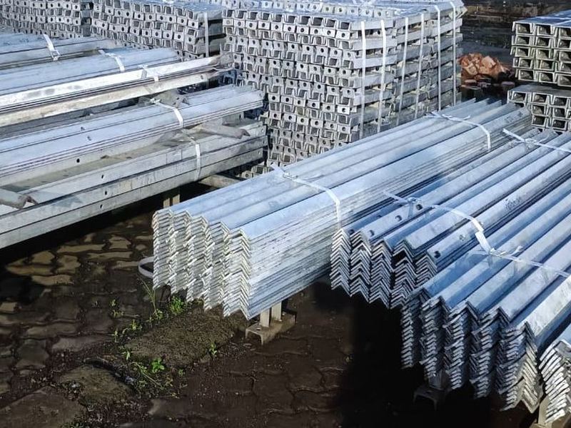 Angle bundles on the paved yard. Galvanized angle and flat sections bundled and stacked on the paved yard, sorted by section before loading.