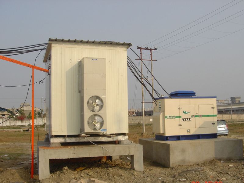 Equipment shelter on a finished base. The equipment shelter and standby set installed on their cast plinths at a completed tower site.